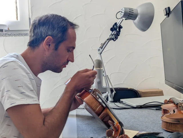 Paul hält eine Geige und arbeitet mit einem Stimmsetzwerkzeug am Instrument